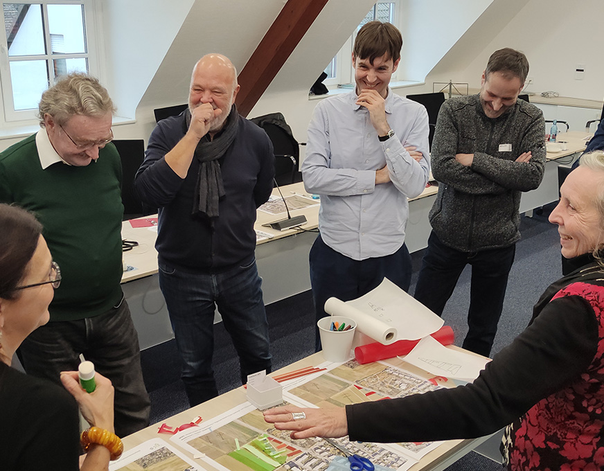 Teilnehmende diskutieren gemeinsam über städtebauliche Planungsunterlagen an einem Tisch