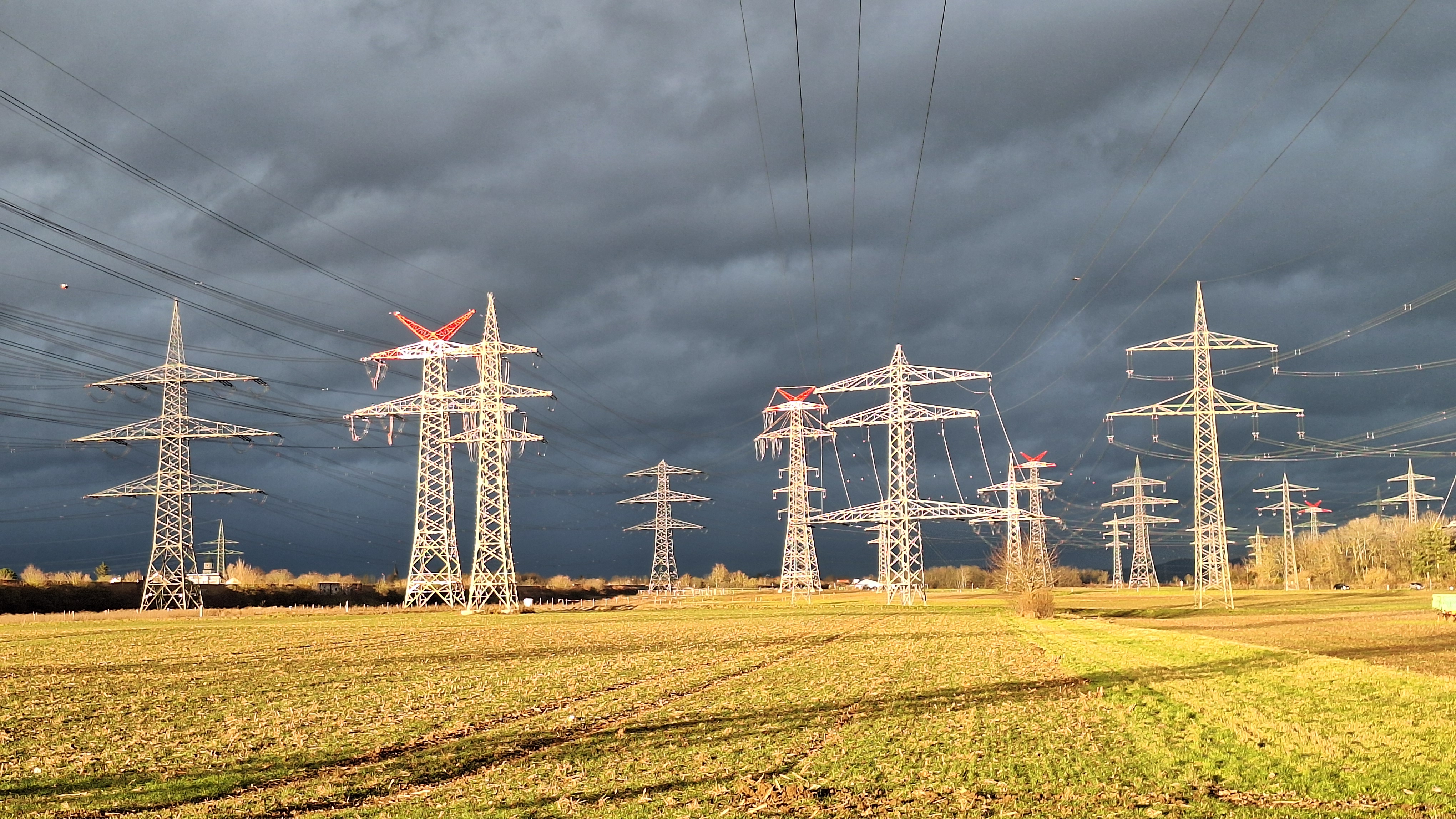 Hochspannungsmasten über einem Feld unter dunklen Gewitterwolken bei Ilvesheim