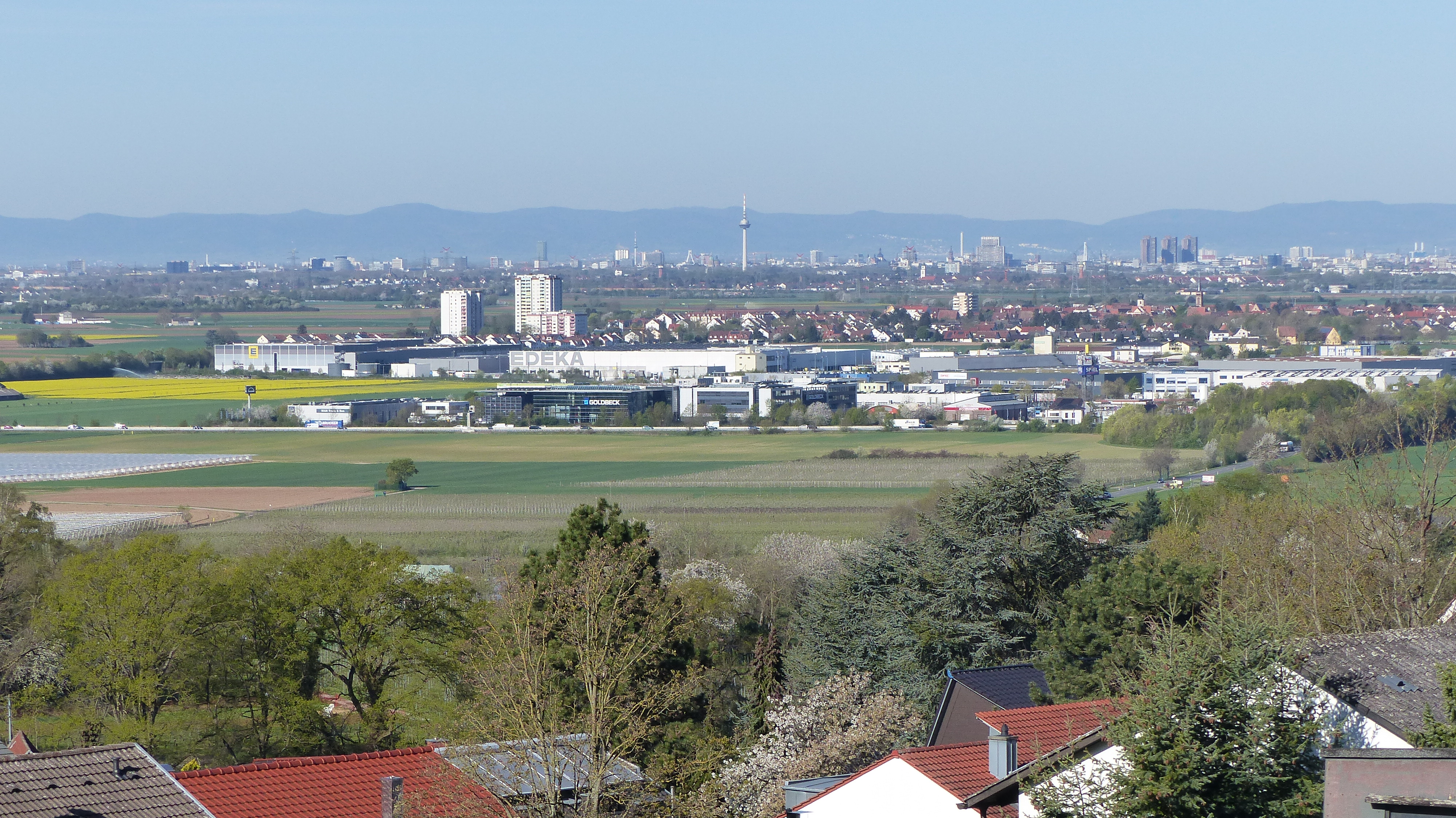 Blick über Felder auf ein Gewerbegebiet mit Industriegebäuden und dahinterliegender Stadt (Hirschberg/Heddesheim)